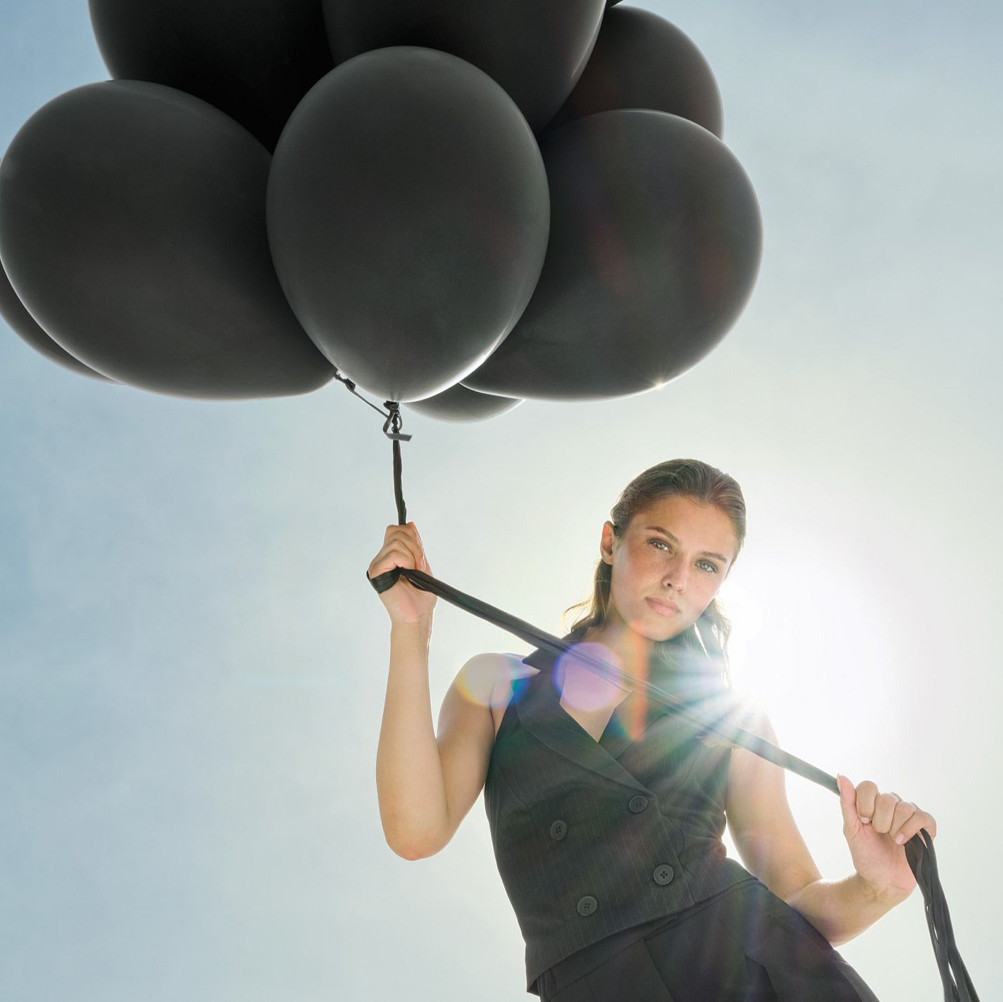 Una donna vestita di nero tiene dei palloncini neri fissati a dei nastri che fluttuano sopra di lei.