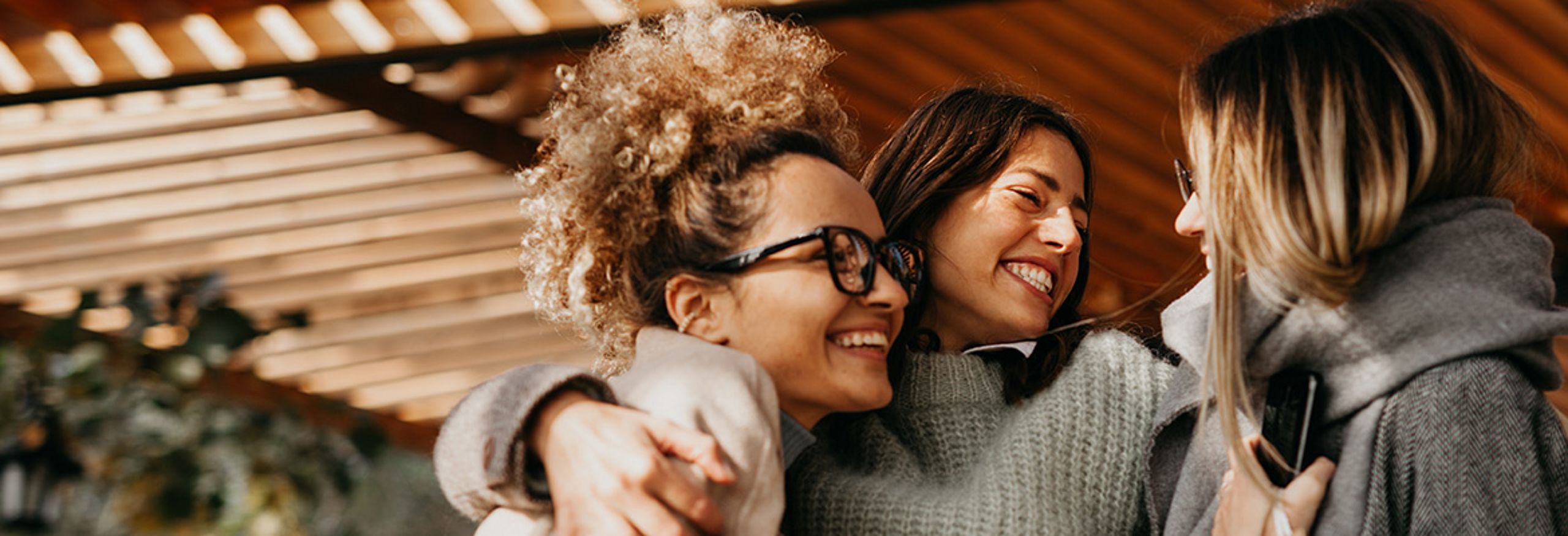 Tre giovani donne sono in piedi insieme, si abbracciano e ridono