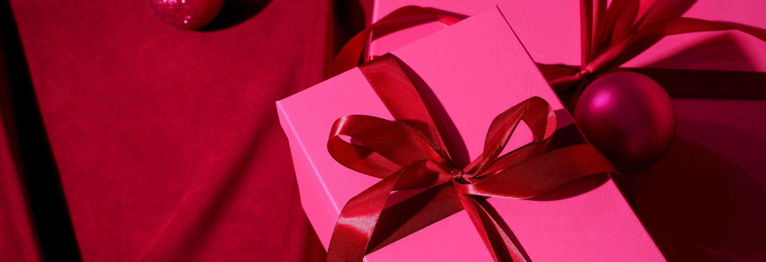 Teaser editoriale per la pubblicità natalizia. L'immagine mostra scatole rosa con un fiocco.