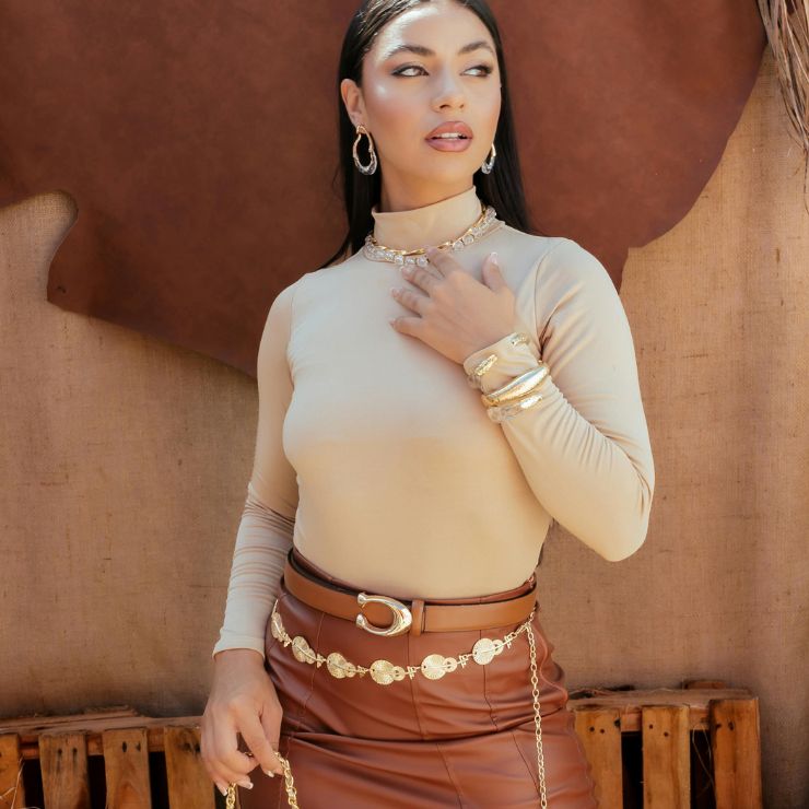 Una donna indossa un maglione a collo alto e una gonna e si mostra con una mano sul collo. L'immagine viene utilizzata per rappresentare la tendenza del colore marrone. 