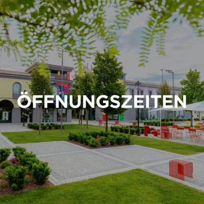 Viene mostrata l'entrata del Palmanova Designer Village. L'immagine riporta inoltre il titolo “Orari di apertura” in tedesco.