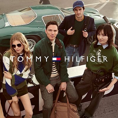 Quattro persone sono appoggiate a un'auto d'epoca e guardano verso la telecamera. Sopra di loro è posizionato il logo Tommy Hilfiger.